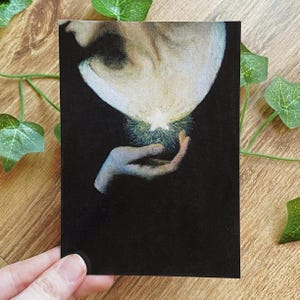 Könnte beinhalten: Ein dunkler, künstlerischer Druck, der ein Gesicht und eine Hand zeigt. Ein helles Licht geht vom Gesicht aus und wird in der Hand gehalten. Das Kunstwerk hat eine Vintage- und ätherische Qualität.
