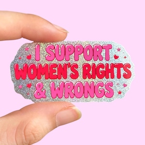 Könnte beinhalten: Ein holografischer Aufkleber mit gewelltem Rand und dem rosafarbenen Text I SUPPORT WOMEN'S RIGHTS & WRONGS. Das Design enthält kleine rosa Herzen und Sterne, die über den schimmernden silbernen Hintergrund verteilt sind und ein lebendiges Aussehen erzeugen.
