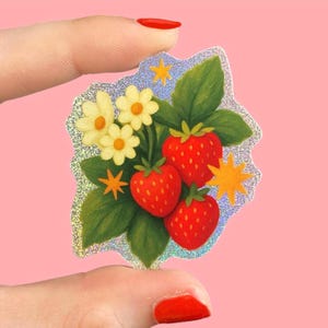 Könnte beinhalten: Ein holografischer Aufkleber mit einem Erdbeer-Design. Der Aufkleber zeigt drei rote Erdbeeren, grüne Blätter, gelbe Blüten und Sternakzente. Er hat einen glitzernden, irisierenden Rand.