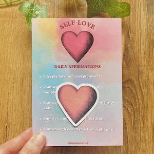 Könnte beinhalten: Eine rechteckige Karte mit pastellfarbenem Aquarellhintergrund, die den Text SELF-LOVE DAILY AFFIRMATIONS und eine Liste von fünf Aussagen enthält. Ein rosa Herzaufkleber ist über dem Text platziert. Die Karte enthält den Namen @louisenkind.