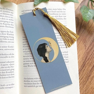 Könnte beinhalten: Blaues Lesezeichen mit goldener Quaste. Das Lesezeichen zeigt eine Illustration von zwei Figuren, die sich in einem Halbmond küssen. Die Website-Adresse "www.louisenkind.com" ist unten aufgedruckt.