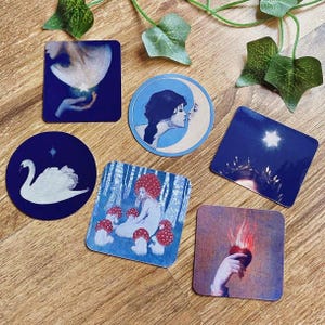 Könnte beinhalten: Eine Sammlung von sechs Kunstdrucken mit himmlischen und skurrilen Designs. Die Drucke zeigen einen Schwan, eine Frau mit dem Mond, eine Figur mit Pilzen und eine Hand, die ein brennendes Herz hält. Die Drucke sind in Blau-, Weiß- und Rottönen gehalten.