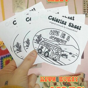 May include: A hand holding several white coloring sheets with a black and white illustration of a van and the text "LIFE IS A JOURNEY". The sheets also have the text "FREE COLORING SHEET WITH EVERY ORDER!"
