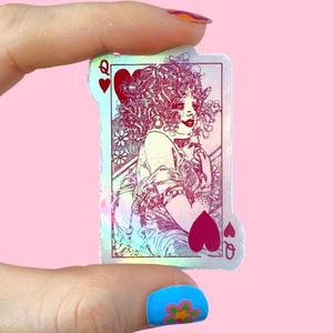 Könnte beinhalten: Holografischer Aufkleber der Herzkönigin Spielkarte. Die Karte zeigt eine Vintage-Illustration einer Frau mit lockigem Haar, einem roten Herzen und dem Buchstaben "Q". Der Aufkleber hat ein rosa und schillerndes Finish.