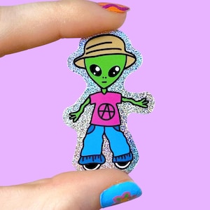 Könnte beinhalten: Ein holografischer Aufkleber mit einem Cartoon-Alien mit grünem Gesicht, das einen beigen Hut, ein rosa Hemd und eine blaue Jeans trägt. Das Hemd hat ein weißes Symbol. Das Alien hat große schwarze Augen und lächelt. Der Aufkleber hat einen glitzernden Rand.