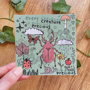Könnte beinhalten: Ein quadratischer, salbeigrüner Aufkleber mit skurrilen Illustrationen von Insekten, Pflanzen und Wetterelementen. Der Aufkleber zeigt einen großen rosa Käfer, einen Marienkäfer, einen Schmetterling und eine Schnecke. Der Text enthält "every creature is precious" und andere Phrasen.