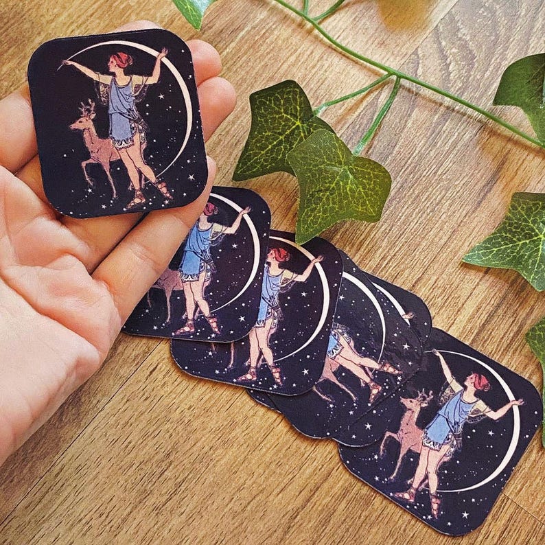 May include: Rectangular stickers featuring a celestial design. Each sticker depicts a woman in a blue dress with a deer, set against a starry night sky and a crescent moon. The woman has red hair and is in a dancing pose.