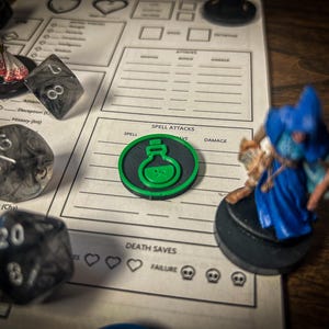 Peut inclure: Une scène de jeu de rôle sur table avec une feuille de personnage, des dés et une figurine. Une icône de potion verte est sur un jeton circulaire noir. Les dés sont translucides avec des chiffres blancs. La figurine est un magicien en robe bleue.