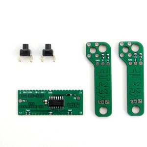 Può includere: Componenti elettronici su sfondo bianco. L'immagine presenta due pulsanti neri, un circuito stampato verde con un circuito integrato e due circuiti stampati verdi con testo giapponese.