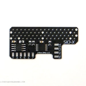 May include: A black circuit board with the text "SIO-X" and "XE XI CICE" printed on it. The board has a grid of holes and several small electronic components.