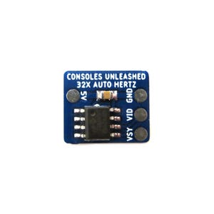 May include: A small, square blue circuit board with the text "CONSOLES UNLEASHED 32X AUTO HERTZ" printed on it. The board has a black integrated circuit chip and several silver-coloured connection points. The background is white.