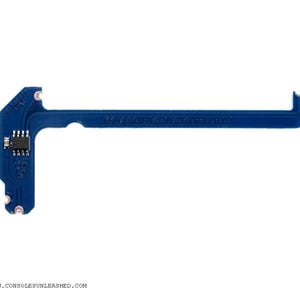 Puede incluir: Una placa de circuito impreso azul con un pequeño chip y una muesca en el extremo. La placa está etiquetada como "Game Over" y "Console Unleashed".