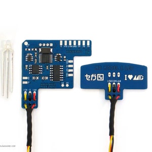 Könnte beinhalten: Zwei blaue elektronische Leiterplatten mit Text und Komponenten, verbunden durch Drähte. Eine Platine trägt die Aufschrift "UNLEASHED MEGA DRIVE". Die andere trägt "MD MODEL 1 LED" mit japanischen Schriftzeichen und "I <3 MD". Ein Satz silberner Stifte ist ebenfalls vorhanden.