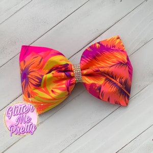May include: A large, vibrant hair bow with a tropical floral pattern in shades of pink, orange, yellow, and purple. The bow is accented with a sparkling rhinestone center. The text "Glitter Me Pretty" is in the lower left corner.