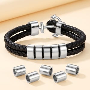 May include: A black braided leather bracelet featuring a silver-toned metal anchor clasp and five cylindrical silver-toned metal beads threaded onto the double-strand band, accompanied by five additional loose cylindrical silver-toned metal beads.