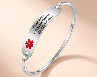 Könnte beinhalten: Ein silberfarbenes medizinisches Notfallarmband aus Metall mit einer flachen, gebogenen Identifikationsplatte. Die Platte zeigt ein rotes medizinisches Stern des Lebens-Symbol und den eingravierten Text: Renee Owens, Asthma and Diabetes, ICE 815-978-8512.