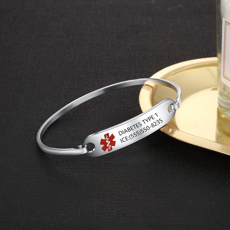 May include: Silver medical alert bracelet with a red medical symbol and the text "DIABETES TYPE 1 ICE:(555)550-8235".