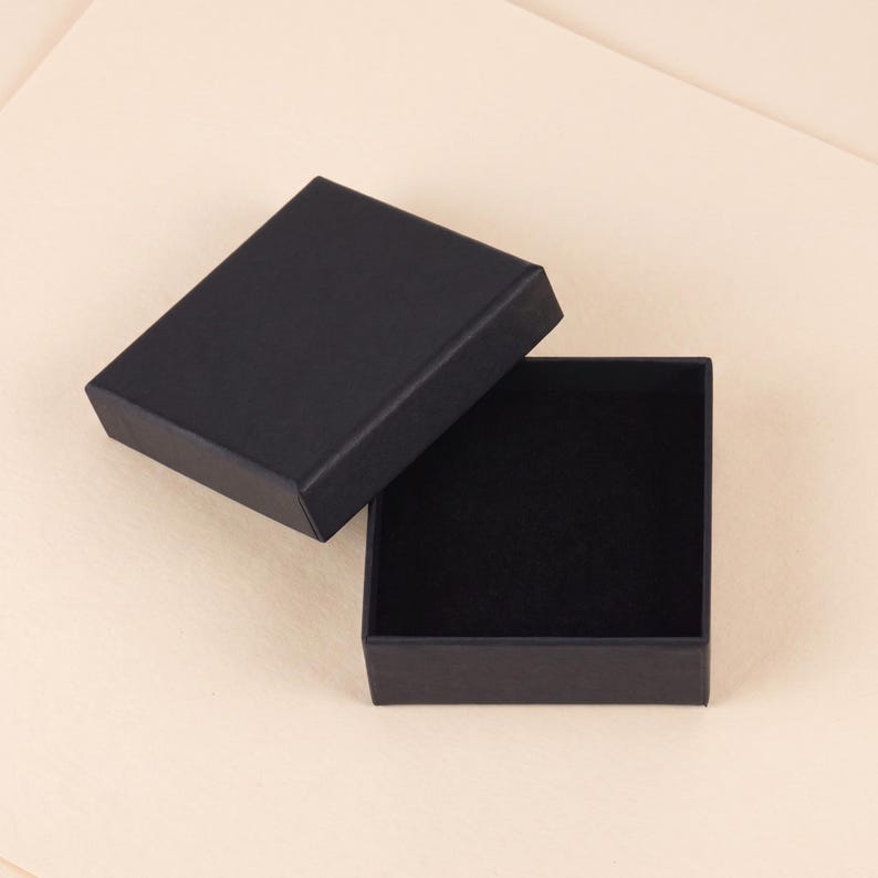 May include: A rectangular black jewelry box with a removable lid. The box features a matte black exterior finish and a deep black velvet-lined interior base, providing a clean and simple storage solution for small items or accessories.