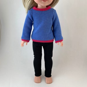 May include: A doll wearing a blue long-sleeved shirt with a pink trim and black leggings.