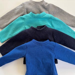 May include: Four long-sleeved shirts in different colors: gray, teal, navy blue, and royal blue. The shirts are stacked on top of each other.