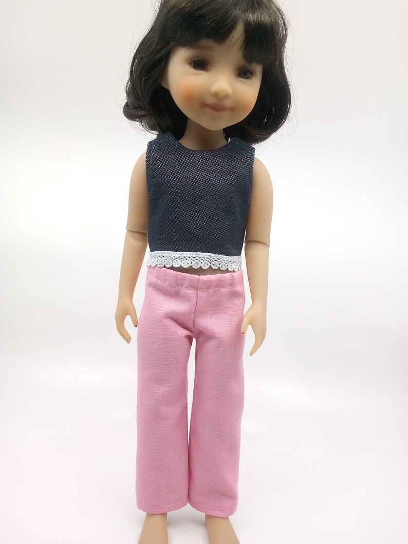 May include: A doll wearing a dark blue denim sleeveless top with white lace trim and pink pants.