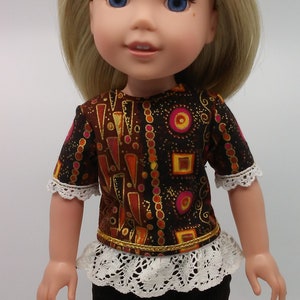 Może przedstawiać: Lalka ubrana w brązową i złotą wzorzystą koszulę z białą koronkową lamówką, białą koronkową falbanką i brązowe spodnie.