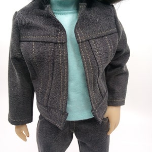May include: A dark gray denim jacket with a light blue t-shirt underneath. The jacket has a pointed collar and a button closure. The t-shirt has a crew neck. The model is wearing dark gray denim pants.