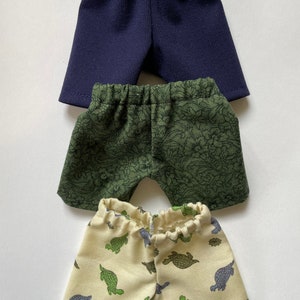 May include: Three pairs of shorts in different colors and patterns. The top pair is navy blue, the middle pair is green with a floral pattern, and the bottom pair is cream with a green turtle pattern.