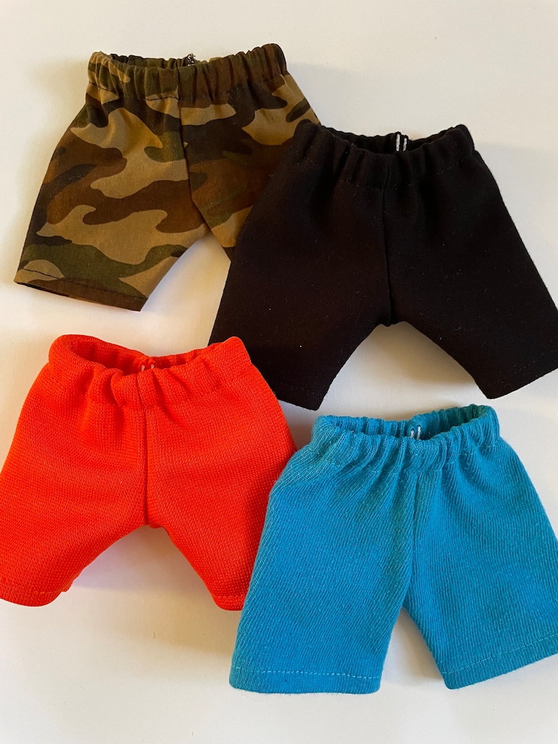 May include: Four pairs of shorts in different colors: camouflage, black, orange, and blue. The shorts are made of a soft, stretchy fabric and have an elastic waistband.