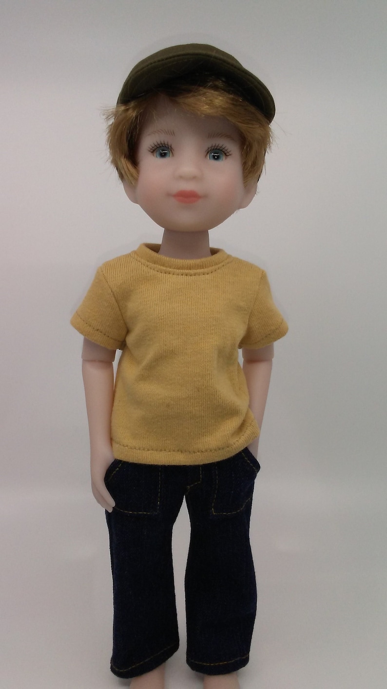 May include: A doll wearing a yellow t-shirt, blue jeans, and a green cap. The doll has blonde hair and blue eyes.