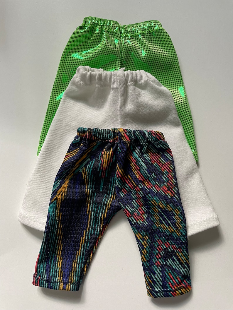 May include: Three pairs of leggings in different colors and patterns. The top pair is green, the middle pair is white, and the bottom pair is black with colorful stripes.