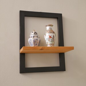 May include: A black framed shelf with a wooden shelf and two decorative porcelain vases. One vase is a tall, slender vase with a floral design. The other vase is a round, squat vase with a lid and a floral design.