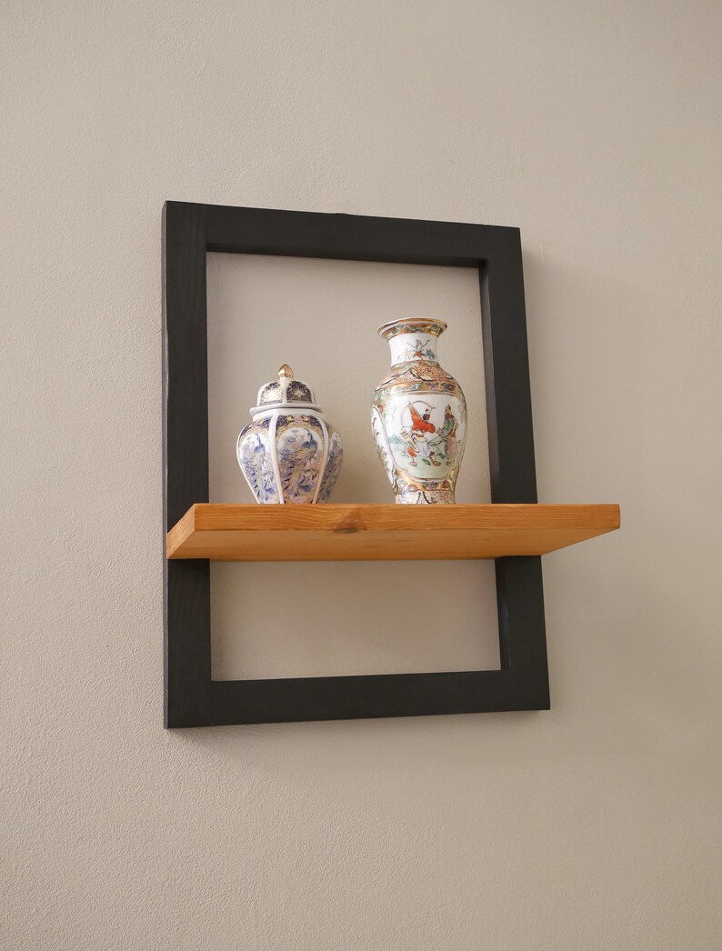 May include: A black framed shelf with a wooden shelf and two decorative porcelain vases. One vase is a tall, slender vase with a floral design. The other vase is a round, squat vase with a lid and a floral design.