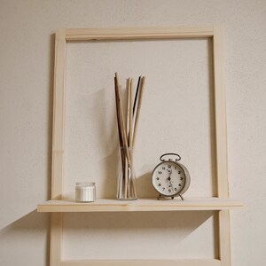 Puede incluir: Una estanter&iacute;a de madera con una vela blanca, un jarr&oacute;n de palitos y un reloj despertador vintage. La estanter&iacute;a est&aacute; unida a un marco de madera.