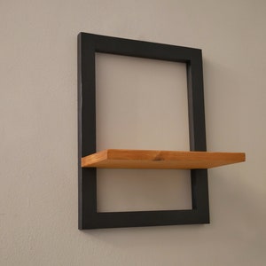 May include: A black metal shelf with a wooden shelf. The shelf is mounted to a white wall.