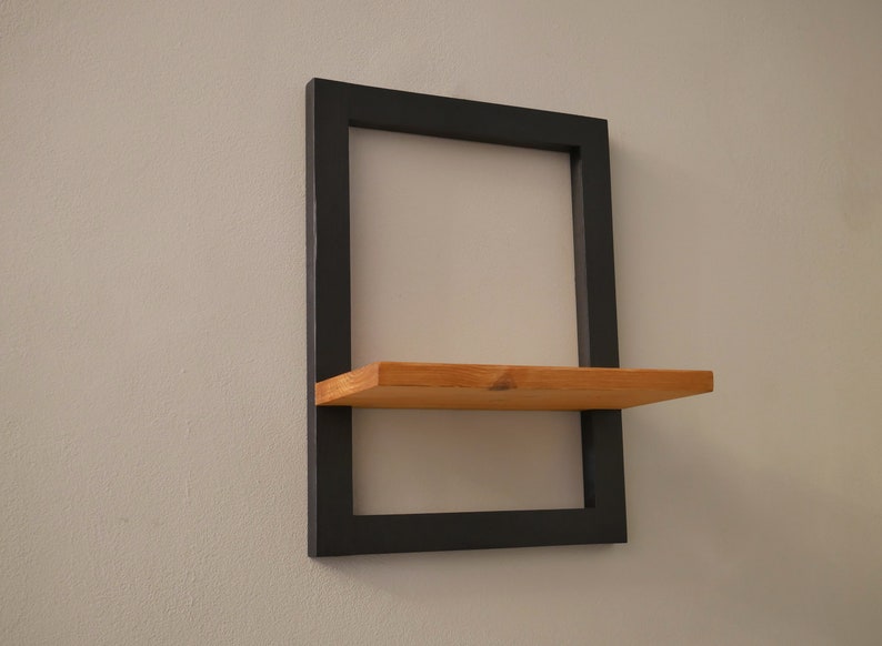 May include: A black metal shelf with a wooden shelf. The shelf is mounted to a white wall.
