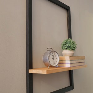 Puede incluir: Una estanter&iacute;a de metal negro con una repisa de madera unida. La estanter&iacute;a est&aacute; decorada con un reloj despertador vintage, una planta en maceta y una pila de libros.