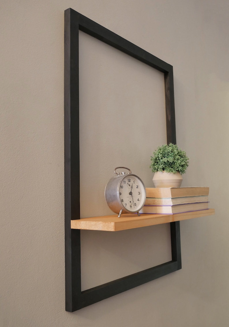 Puede incluir: Una estanter&iacute;a de metal negro con una repisa de madera unida. La estanter&iacute;a est&aacute; decorada con un reloj despertador vintage, una planta en maceta y una pila de libros.