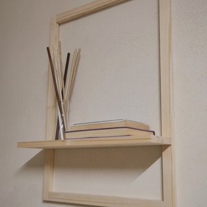 Puede incluir: Una estanter&iacute;a de madera con un marco alrededor. La estanter&iacute;a est&aacute; fijada a una pared y tiene algunos libros y un jarr&oacute;n con palitos.