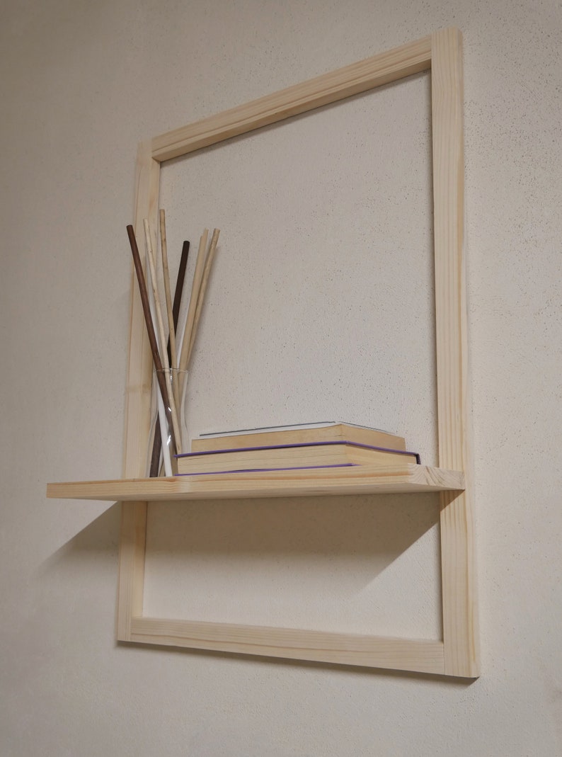 Puede incluir: Una estanter&iacute;a de madera con un marco alrededor. La estanter&iacute;a est&aacute; fijada a una pared y tiene algunos libros y un jarr&oacute;n con palitos.