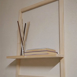 Puede incluir: Una estanter&iacute;a de madera con un marco alrededor. La estanter&iacute;a est&aacute; montada en una pared y tiene algunos libros y un jarr&oacute;n con palos.
