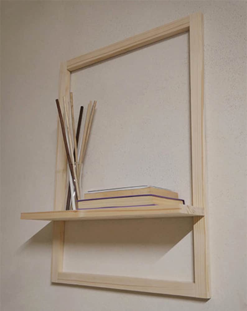 Puede incluir: Una estanter&iacute;a de madera con un marco alrededor. La estanter&iacute;a est&aacute; montada en una pared y tiene algunos libros y un jarr&oacute;n con palos.