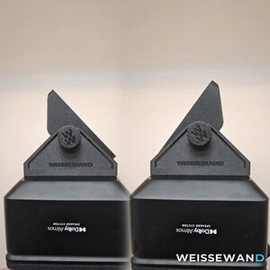 Könnte beinhalten: Zwei schwarze Lautsprechersysteme mit dreieckiger Oberseite und dem Text "WEISSEWAND". Die Lautsprecher haben ein Dolby Atmos-Logo und ein stilisiertes "W"-Emblem. Die Basis der Lautsprecher ist rechteckig.