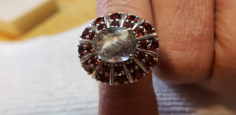 Centeral oval rutilated quartz surrounded by smaller and larger garnets in inner and outer stones Size 7. Platinum over sterling silver