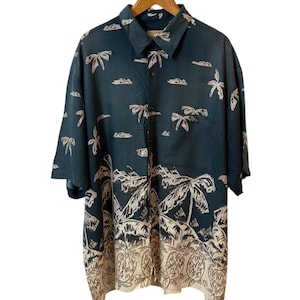 Puede incluir: Camisa abotonada de color verde azulado oscuro con un estampado tropical de palmeras y nubes. La camisa de manga corta tiene un diseño de borde beige y blanco en la parte inferior. La camisa está colgada en una percha de madera.