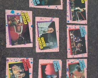 May include: A collection of eight rectangular trading cards featuring various photographs of Cyndi Lauper. Each card has a pink border with blue and purple paint splatter designs and a yellow or blue label reading Cyndi Lauper.