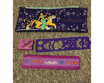 May include: A purple pencil case featuring Jasmine and Rajah from Aladdin, a small pink eraser with the Aladdin logo, a purple stencil ruler with various shapes, and a 15 cm purple ruler with Aladdin branding and colorful icons.