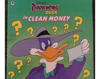 May include: A square children's book cover titled Disney's Darkwing Duck in CLEAN MONEY. The illustration features the purple-clad character wearing a wide-brimmed hat, holding a blank white paper, surrounded by yellow question marks on green.