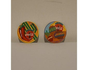 May include: Two round Coca-Cola themed pins. One pin features a red chili pepper and the text "It's always a good time". The other pin has a desert theme with the text "It's always taco time".