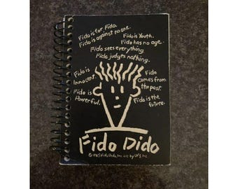May include: A black spiral-bound notebook featuring a white line drawing of the character Fido Dido. The cover includes the text: Fido is for Fido. Fido is against no one. Fido is Youth. Fido has no age. Fido sees everything. Fido judges nothing. Fido is Innocent. Fido comes from the past. Fido is Powerful. Fido is the future. Fido Dido. 1985 Fido Dido, Inc. Lic by UFS, Inc.